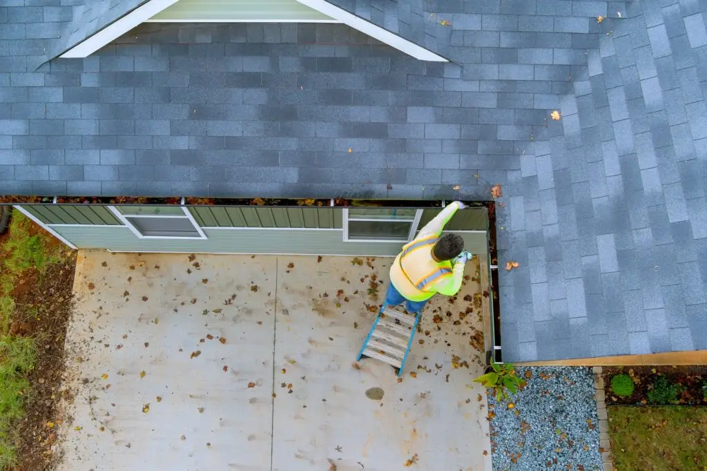 An employee is cleaning a clogged roof gutter drain with dirt, debris, fallen leaves
